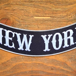 May include: Black and white embroidered patch with the text "NEW YORK" in a curved shape.