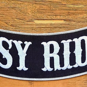 May include: Black and white embroidered "EASY RIDER" patch with a curved shape. The patch is made of fabric and has a white border.