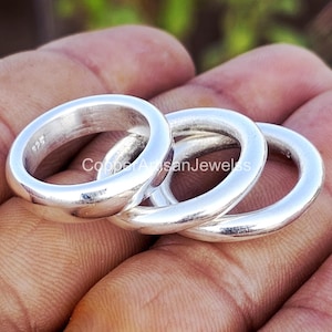 Puede incluir: Se muestran tres anillos de plata con un diseño liso y redondeado. Los anillos están apilados, mostrando su superficie pulida. Es probable que los anillos estén hechos de plata de ley, como indica el sello "925" visible en uno de los anillos. Los anillos son una joya sencilla y elegante.