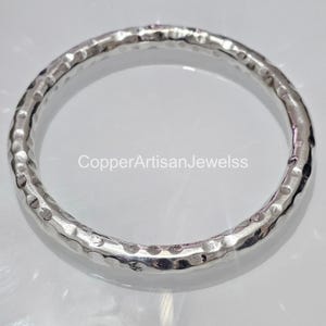 May include: A silver hammered bangle bracelet. The bracelet is smooth and shiny, with a hammered texture.