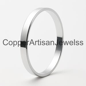 Peut inclure: Une bague en métal argenté poli avec une surface plate et lisse et un design de bande simple. Le texte CopperArtisanJewelss est superposé au centre de la bague. La bague a une finition réfléchissante et une forme circulaire nette.