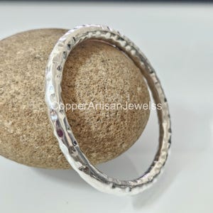 May include: A silver hammered bangle bracelet. The bracelet is smooth and shiny, with a hammered texture. It is a simple and elegant design.