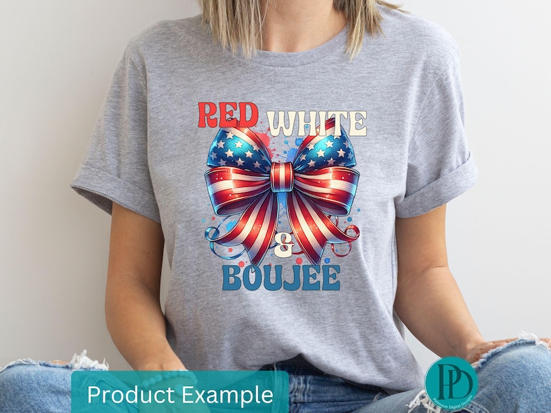 May include: A light gray t-shirt featuring a patriotic bow design in red, white, and blue. The bow is adorned with stars and stripes, with the words "RED WHITE & BOUJEE" in a stylized font.