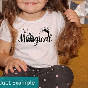 May include: A white t-shirt with a black silhouette of a castle and a fairy with the text "Magical" printed on it. The shirt is being worn by a child.