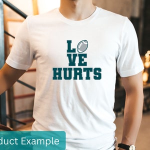 K&ouml;nnte beinhalten: Wei&szlig;es T-Shirt mit einem blauen und grauen Football-Motiv und dem Text "LOVE HURTS".