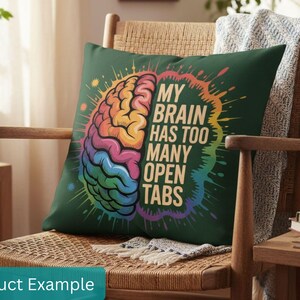 May include: A dark green throw pillow with a colorful brain graphic and the text "MY BRAIN HAS TOO MANY OPEN TABS." The brain illustration features rainbow colors. The pillow is on a wooden chair with a woven seat.