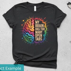 May include: Dark gray t-shirt with a colorful brain graphic. The brain is split into two halves, with one side in warm colors and the other in cool colors. Text reads "MY BRAIN HAS TOO MANY OPEN TABS".