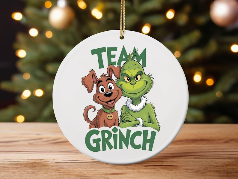 K&ouml;nnte beinhalten: Wei&szlig;er Keramik-Weihnachtsschmuck mit dem Grinch und dem Hund Max. Der Grinch ist gr&uuml;n mit einem wei&szlig;en Fellkragen, und Max ist braun. Die Worte "Team Grinch" sind gr&uuml;n gedruckt.
