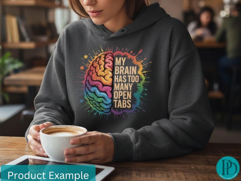 May include: Dark gray hoodie with a colorful brain graphic. The graphic features a rainbow-colored brain with the text "MY BRAIN HAS TOO MANY OPEN TABS". The hoodie is worn by a person holding a white coffee cup.