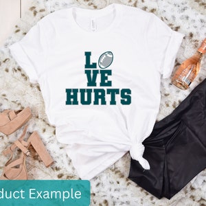 K&ouml;nnte beinhalten: Wei&szlig;es T-Shirt mit dem Text "LOVE HURTS" in Gr&uuml;n und einer Fu&szlig;ballgrafik.