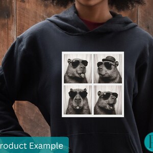 May include: Black hoodie with a square graphic featuring four black and white images of a capybara wearing sunglasses and a hat. The words "Product Example" are at the bottom.