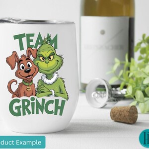 K&ouml;nnte beinhalten: Ein wei&szlig;er, stieloser Weinglasbecher mit einem gr&uuml;nen "Team Grinch"-Motiv mit dem Grinch und Max. Eine Weinflasche, ein Korken und ein Korkenzieher befinden sich im Hintergrund.