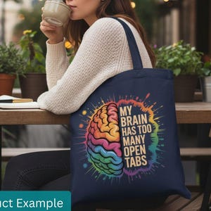 May include: Navy blue tote bag featuring a colorful brain graphic with the text "MY BRAIN HAS TOO MANY OPEN TABS." The brain illustration is in rainbow colors. The bag has a dark blue handle.