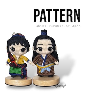 Puede incluir: Dos muñecos chibi de ganchillo, uno con un atuendo amarillo y verde, el otro con una túnica marrón, tomados de la mano. Los muñecos tienen pelo negro y están sobre bases de madera. La palabra "PATTERN" y "Chibi Pursuit of Jade" se muestran encima.