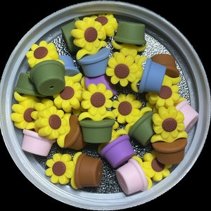 May include: A collection of colorful, miniature flower pot charms with a sunflower design. The charms are made of silicone and have a variety of colors, including blue, green, red, yellow, and white.