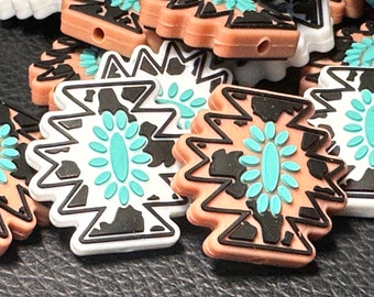 May include: A close-up of several colorful, geometric-shaped silicone charms with a black and white cow print design and turquoise accents. The charms have a zig-zag pattern around the edges.