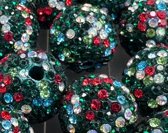 May include: Close-up of several dark green, spherical beads encrusted with colorful rhinestones. The rhinestones are red, blue, green, and clear, creating a sparkling effect. The beads appear to be for jewelry making.