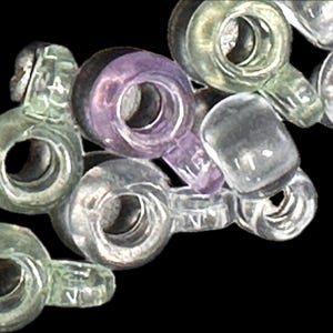 May include: Close-up of a collection of clear, translucent glass beads with a loop and a small tab. Some beads have a slight tint of green or purple. The beads are scattered against a black background.