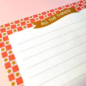 May include: A white notepad with gold lined paper and a red and white checkered border. The top of the notepad has a gold banner with the text "ALL THE THINGS".