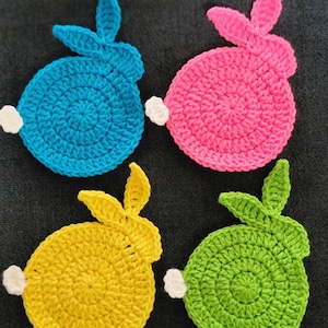 May include: Four crocheted bunny coasters in blue, pink, yellow, and green. Each coaster has a white tail.