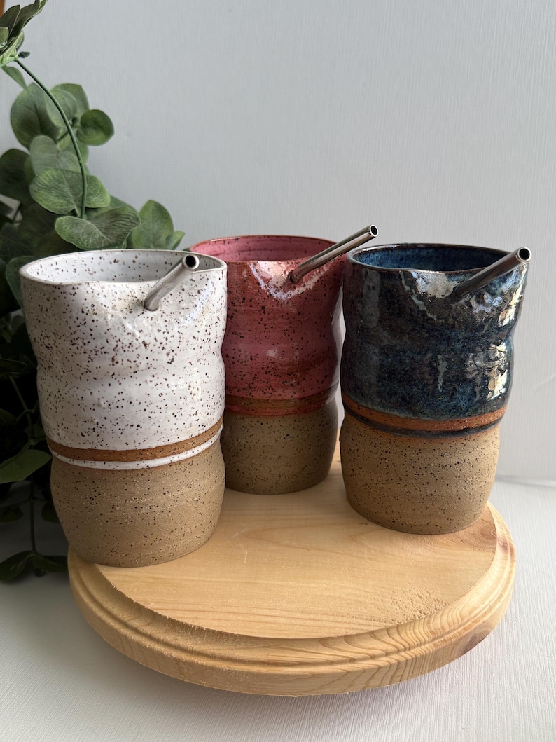 Puede incluir: Tres tazas de cer&aacute;mica con esmalte marr&oacute;n moteado y una banda marr&oacute;n alrededor de la parte superior. Cada taza tiene una pajita de acero inoxidable y es de un color diferente: blanco, rosa y azul.