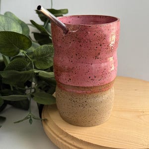 Puede incluir: Una taza de cer&aacute;mica rosa y marr&oacute;n con una pajita de acero inoxidable. La taza tiene un esmalte moteado y una forma redondeada.