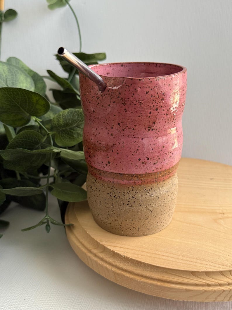 Puede incluir: Una taza de cer&aacute;mica rosa y marr&oacute;n con una pajita de acero inoxidable. La taza tiene un esmalte moteado y una forma redondeada.