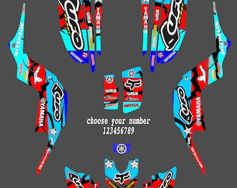 Könnte beinhalten: Ein Satz blauer, roter und schwarzer Motocross-Grafikaufkleber mit dem Wort "UFO" in einer blauen und weißen Schriftart. Die Aufkleber zeigen verschiedene Sponsoren, darunter Fox, Rockstar, Motul und WPS. Die Aufkleber sind für ein Yamaha-Motorrad konzipiert. Der Text "Wähle deine Nummer 123456789" ist enthalten.