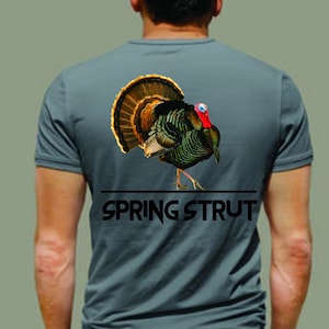 Könnte beinhalten: Ein graues T-Shirt mit einem Aufdruck einer Pute auf der Rückseite. Der Text "SPRING STRUT" ist unter der Pute gedruckt.