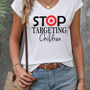 May include: White t-shirt with a black and red graphic that says "STOP TARGETING Children" with a red bullseye in the middle of the word "STOP".