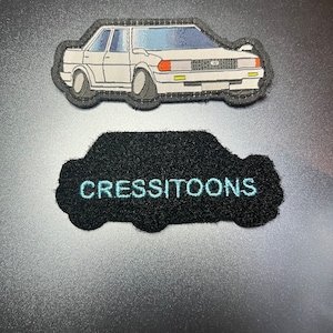 May include: White car embroidered patch with black stitching and a black car-shaped patch with the text "CRESSITOONS" in light blue embroidery.