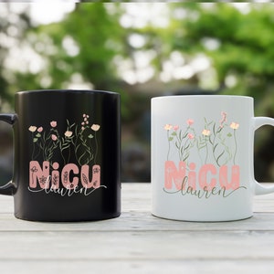 May include: Two ceramic coffee mugs with black and white backgrounds. Both mugs feature a floral design with pink flowers and green stems. The text "NICU Lauren" is printed on both mugs.