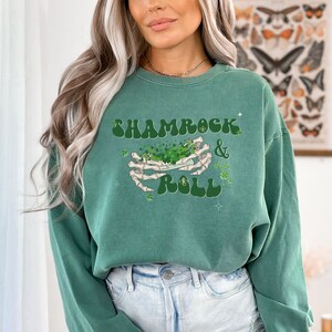 May include: Light green sweatshirt with a graphic of a skeleton hand holding a shamrock and the text "Shamrock & Roll" in a retro font.