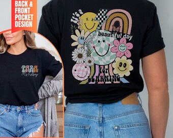 May include: Black t-shirt with a colorful graphic design featuring a rainbow, smiley faces, flowers, and the text "It's a beautiful day for learning".