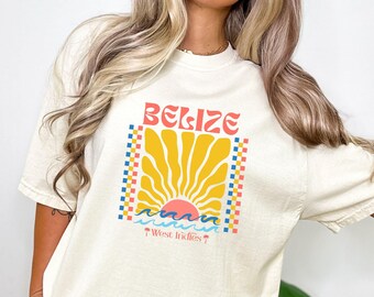 Könnte beinhalten: Cremefarbenes T-Shirt mit einem Grafikdesign mit dem Wort "BELIZE" in Rot und Orange, einem gelben Sonnenaufgang und blauen Wellen. Der Text "West Indies" steht darunter. Das Shirt hat kurze Ärmel und einen Rundhalsausschnitt.