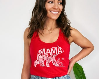 May include: Red tank top with a white floral bear design and the word "MAMA" inside the bear. The model is wearing denim shorts.
