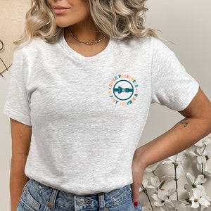 May include: A gray t-shirt with a colorful circle graphic that says "Child Passenger Safety Technician". The graphic features a blue seatbelt buckle.