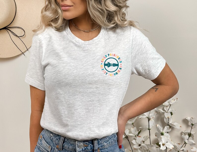 May include: A gray t-shirt with a colorful circle graphic that says "Child Passenger Safety Technician". The graphic features a blue seatbelt buckle.