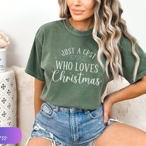 Puede incluir: Una camiseta verde con el texto "Just a CPST who loves Christmas" en letras blancas. La camiseta tiene un aspecto desgastado y la lleva puesta una persona.
