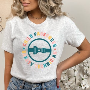 May include: A gray t-shirt with a colorful circle graphic that says "Child Passenger Safety Technician". The graphic features a blue seatbelt buckle.