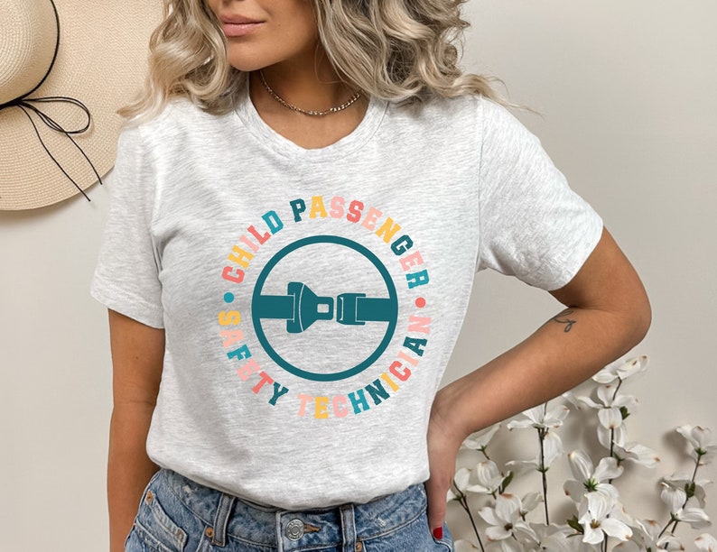 May include: A gray t-shirt with a colorful circle graphic that says "Child Passenger Safety Technician". The graphic features a blue seatbelt buckle.