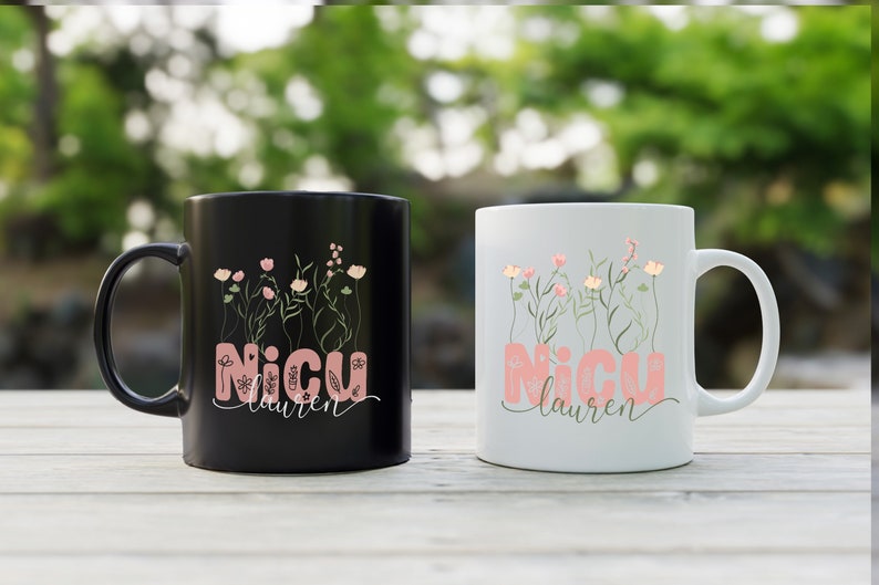 May include: Two ceramic coffee mugs with black and white backgrounds. Both mugs feature a floral design with pink flowers and green stems. The text "NICU Lauren" is printed on both mugs.
