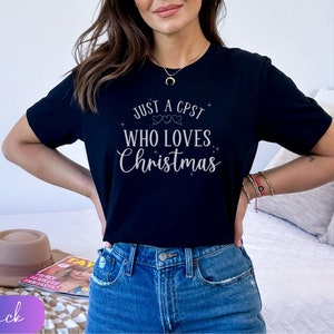 Puede incluir: Una camiseta negra con el texto "Just a CPST who loves Christmas" en letras plateadas brillantes.