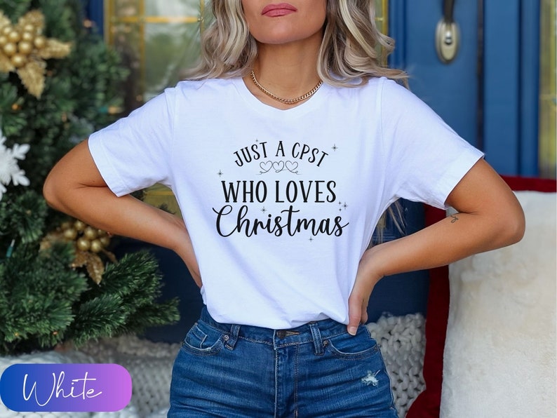 Puede incluir: Camiseta blanca con el texto "Just a CPST who loves Christmas" en letras negras con dos peque&ntilde;os corazones sobre la palabra "loves".
