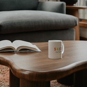 May include: A white ceramic mug featuring the colorful number sequence 5423 printed in red, orange, green, and blue, with the cursive text sturgeon bay wisconsin positioned directly underneath the numbers on the side of the mug.