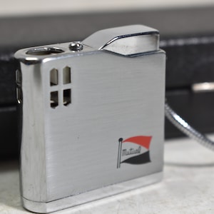 May include: Silver lighter with a red, white and black flag with the word "Mutual" on it. The lighter has a chain attached to it.