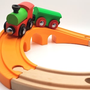 Puede incluir: Un tren de juguete de madera verde y rojo con un solo vagón va por un puente de madera con piezas de vía naranja.
