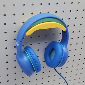 以下が含まれることがあります： ヘッドバンドに黄色と緑のアクセントが付いた青色のオーバーイヤーヘッドホン。ヘッドホンには青色のコードとイヤーカップが付いています。ヘッドホンは白いペグボードに吊り下げられています。