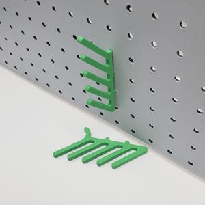 May include: Green plastic pegboard hooks, designed to hold items on a pegboard wall. The hooks are in the shape of a comb with five prongs.