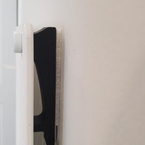 Könnte beinhalten: Eine schwarz-weiße Heizkörperhalterung ist an einer weißen Wand montiert. Die Halterung dient dazu, einen Heizkörper zu befestigen. Der Heizkörper ist weiß und hat eine Reihe von vertikalen Schlitzen.